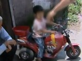 Toddler drives toy motorbike along busy road