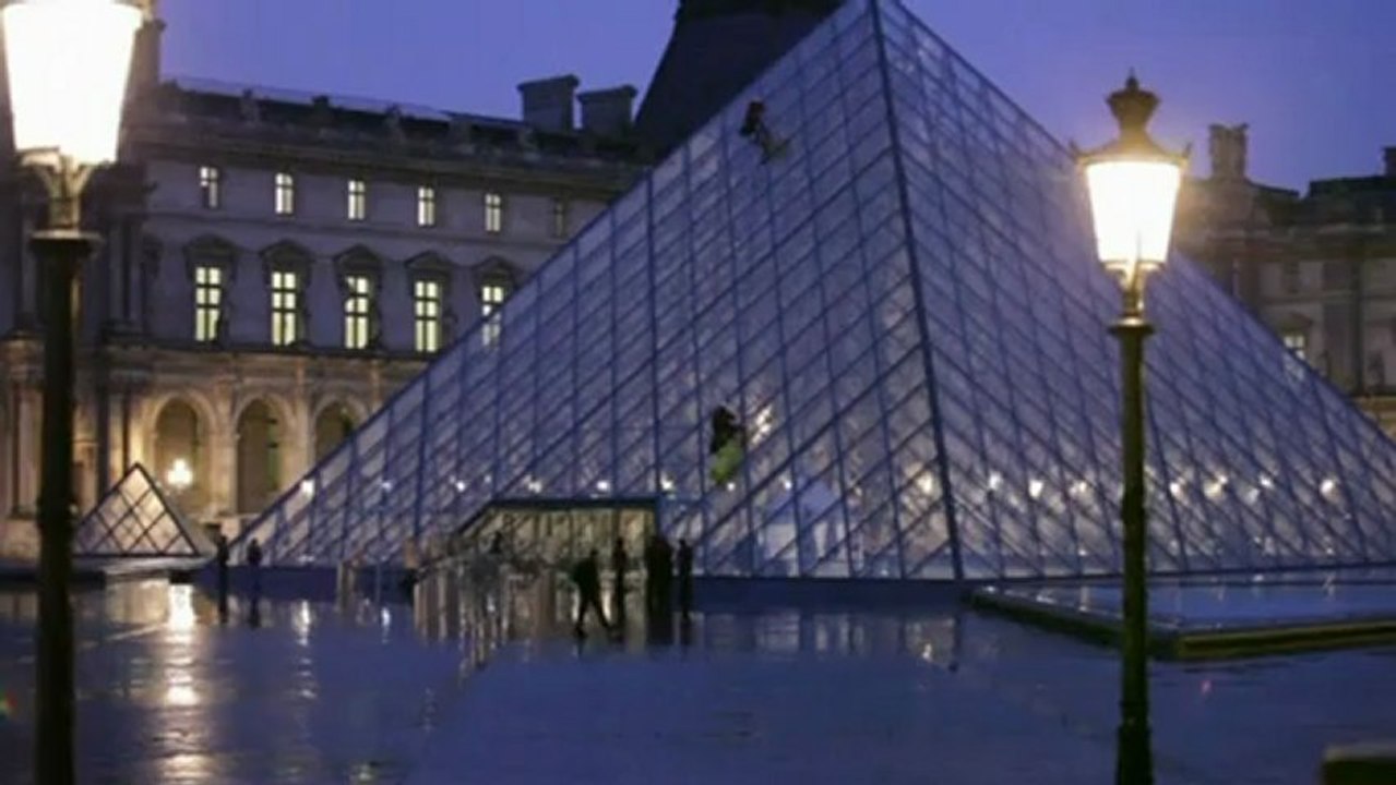 Activists scale the side of the Louvre Museum i...