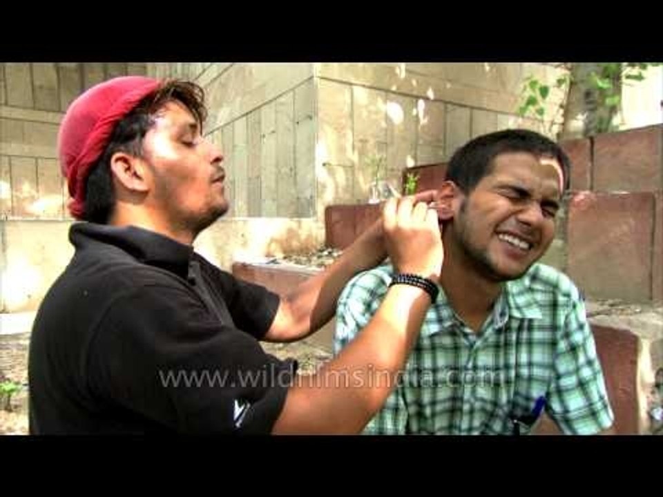 This Ear cleaner causes his client to grimace with both relief and pain!