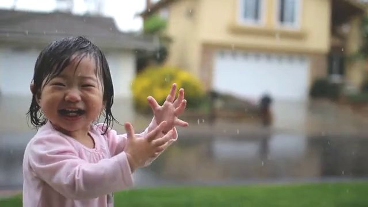Une petite fille découvre la pluie et joue sous les gouttes... Trop mignon!