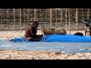 An old fisherman sits, mending his fishing net at Frazerganj