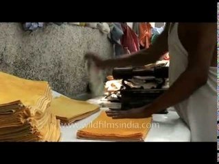 A man irons clothes using an iron heated by charcoal