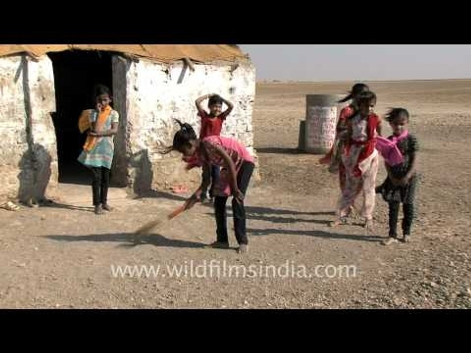 Girl sweeps outside her desert hut...