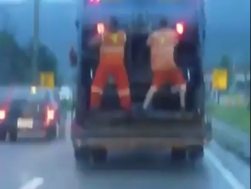 Deux eboueurs dansent sur leur camion poubelle
