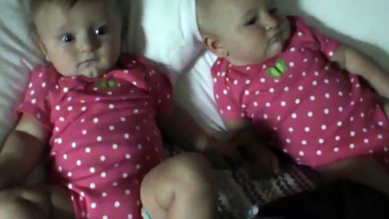 One baby blows raspberries to make the other baby laugh. Adorable overload.