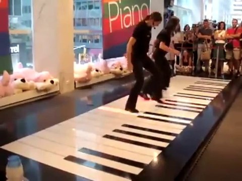 Two people playing Toccata in D Minor on a floor giant piano.