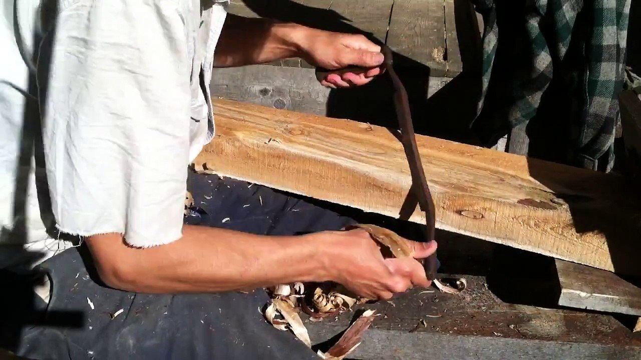 using a shavehorse and a drawknife to remove some bark from a cedar beam