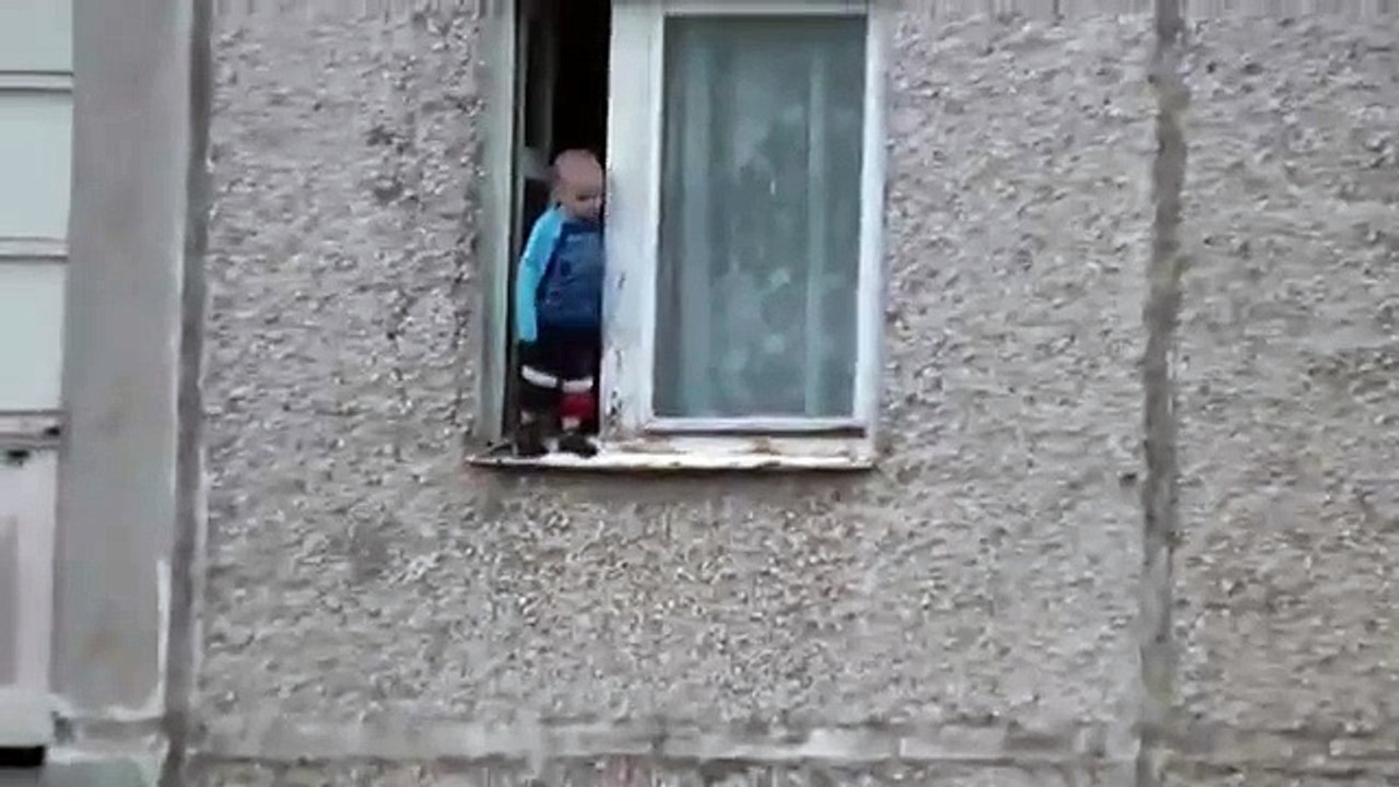 Un enfant joue sur le bord d'une fenêtre au 8ème étage