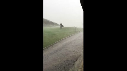 Golfer struggles against the wind as storm hits golf course