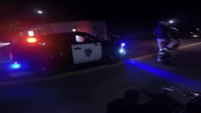Un motard s'amuse à faire du stunt devant une voiture de police