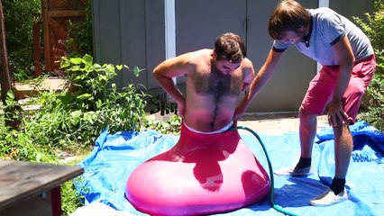 Grown man enters giant water balloon and pops it in slow motion
