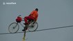 Martial artist rides bike on slack line high in the air