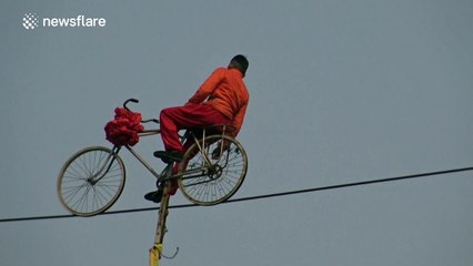 Martial artist rides bike on slack line high in the air