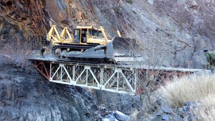 Огромный бульдозер без водителя по краю маленького моста