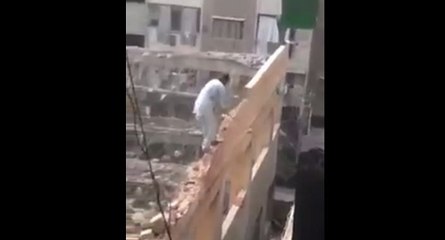 Un homme au-dessus du vide détruit un mur à coup de masse