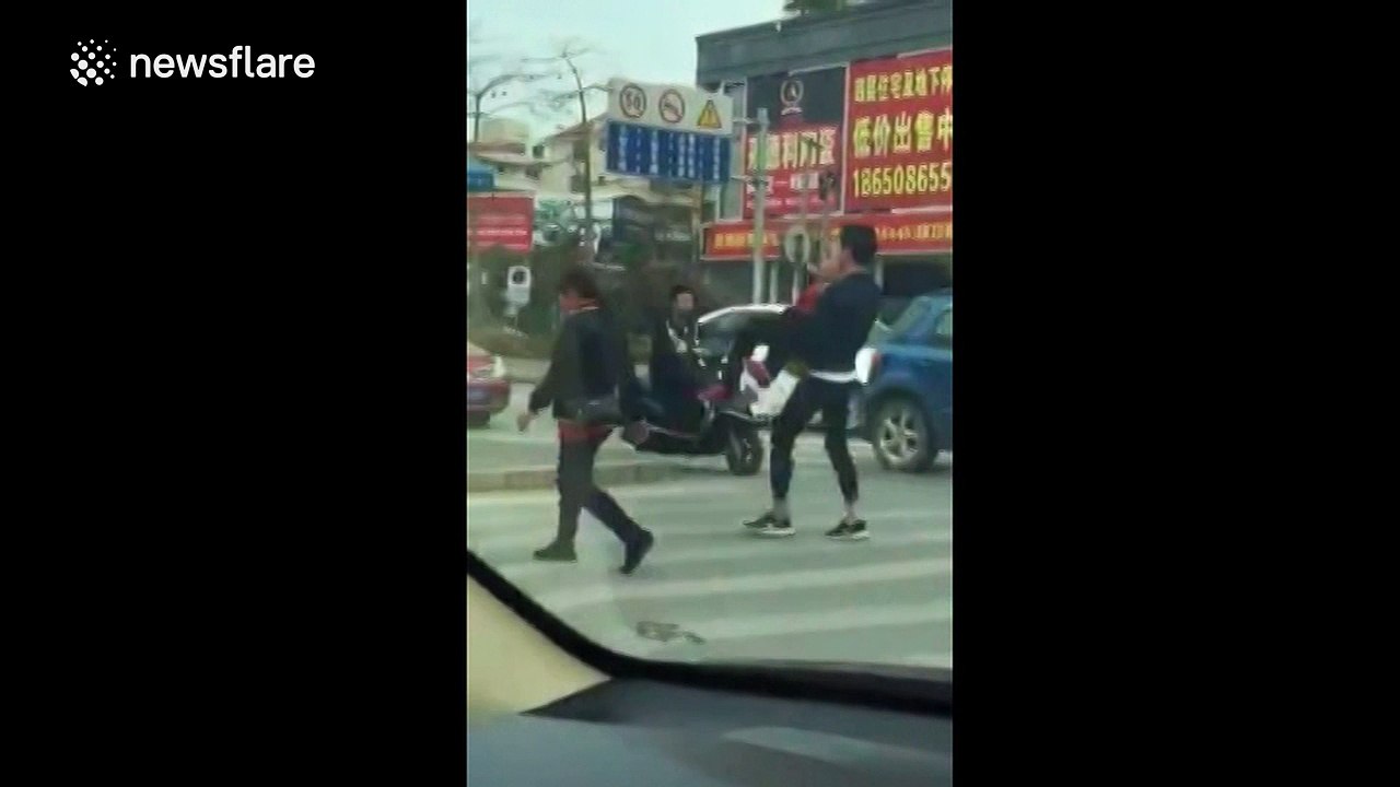 Young man picks up elderly lady to help her cross busy road