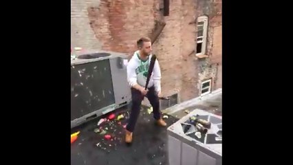 Un homme joue au baseball avec une bouteille de bière sur un toit