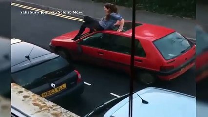 Woman stands on car roof smashing it