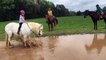 Un poney fait trempette dans une flaque d'eau avec une enfant sur son dos