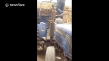 Man drives tractor backwards with one foot on steering wheel