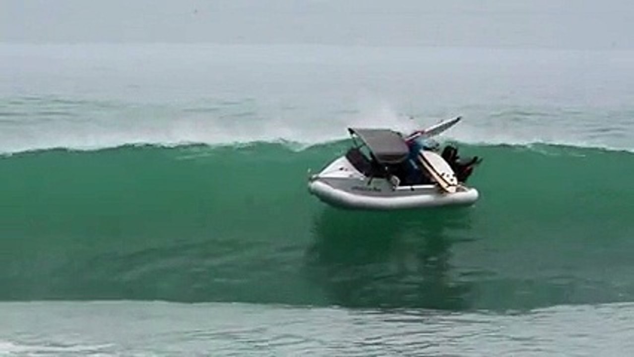 Une vague fait retourner un bateau d'un surfeur.