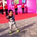 Un enfant chinois répète la chorégraphie des danseuses derrière lui et il danse très bien pour son âge