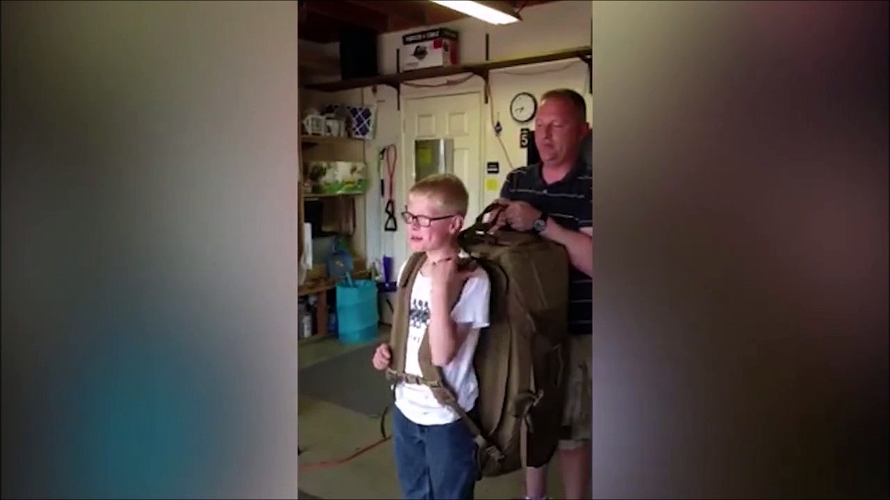 Ce gamin essaie de soulever le sac à dos d'un soldat...
