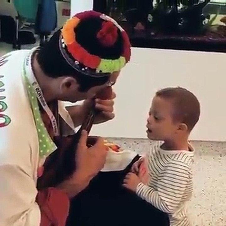 Homem com alguns acessórios na cara toca viola para ver criança com "síndrome de down" feliz