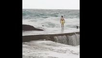 Un jeune saute dans l’eau près des rochers alors que la mer est déchaînée