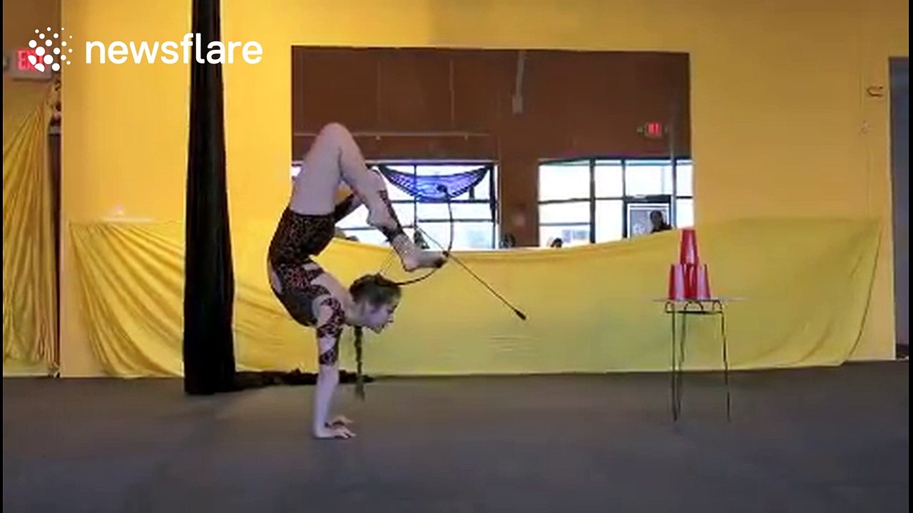 Contortionist fires bow-and-arrow while doing a handstand