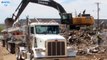 Deere 470G excavator loading debris into a double big rig dump truck on a windy day construction site