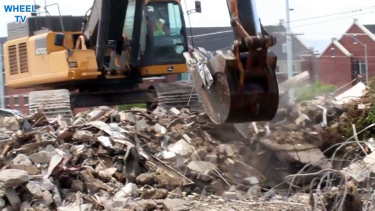 Deere 470G Excavator on top of a big pile of debris from a torn down building loading a side tipping