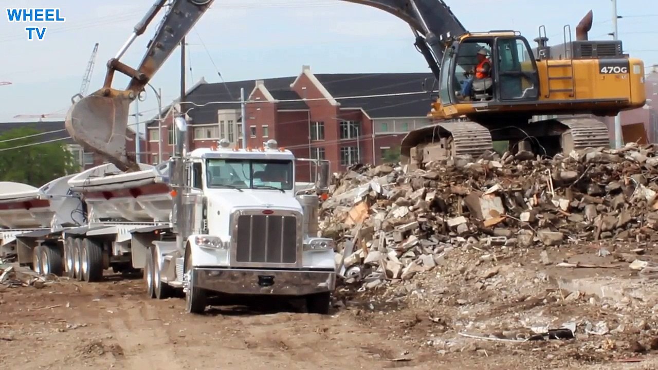 Deere 470G Excavator on top of a pile of debris loading into a double big rig dump truck close up