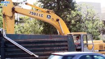 Deere 790ELC excavator loading a blue dump truck and digging a trench on a road construction site