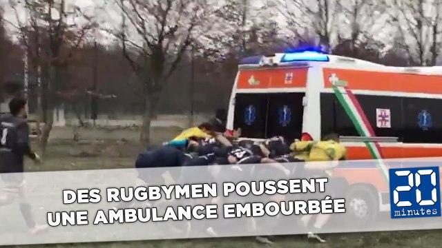 Des rugbymen poussent une ambulance embourbée à côté d'un terrain