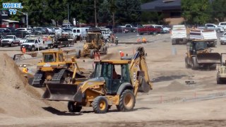 Backhoe digging with many work trucks working all around including a bulldozer loader, construction machine