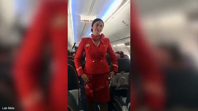 Stjuardesa mundohet ta mbajë të qeshurën derisa demostron udhëzimet e sigurisë