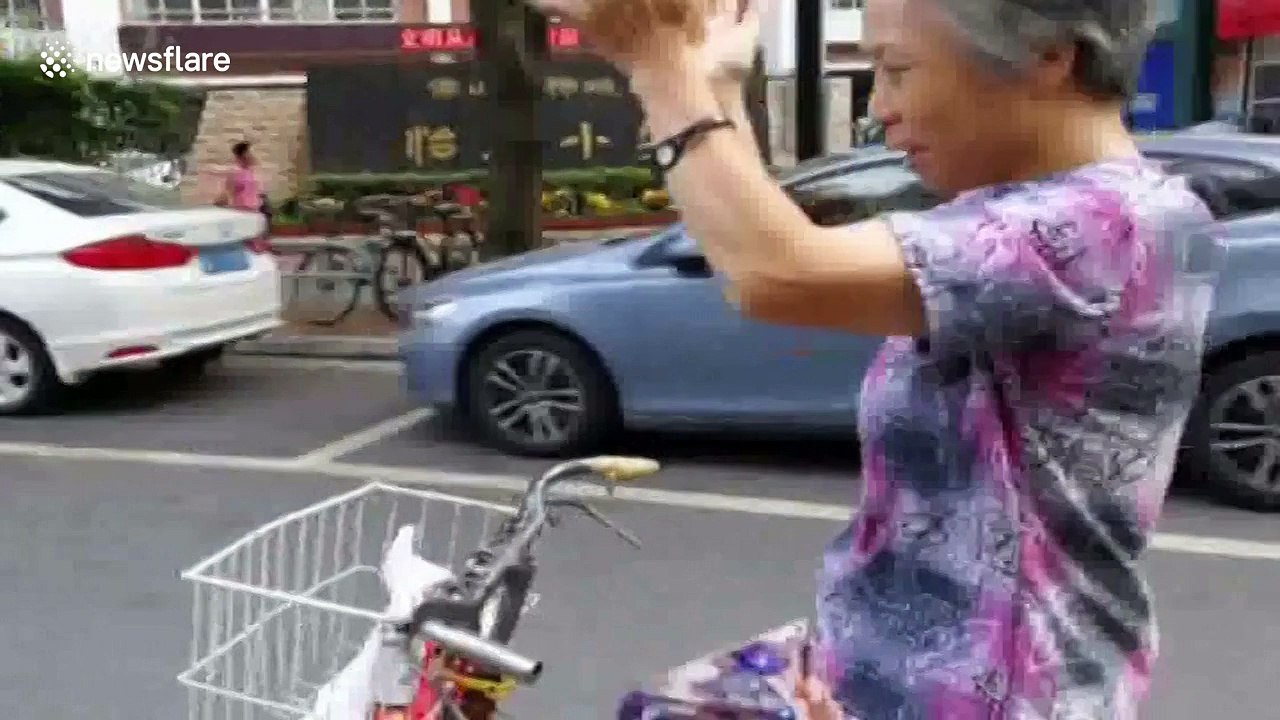 Elderly woman claps her hands in the air while riding a bike
