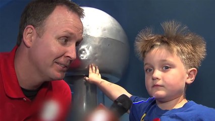 Un enfant avec une main posée sur une bobine Tesla se fait interviewé