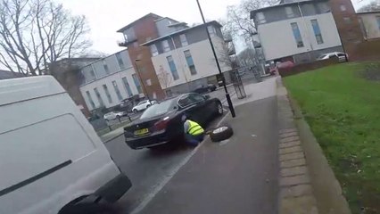Un cycliste tombe sur un homme qui réparait la roue de sa voiture