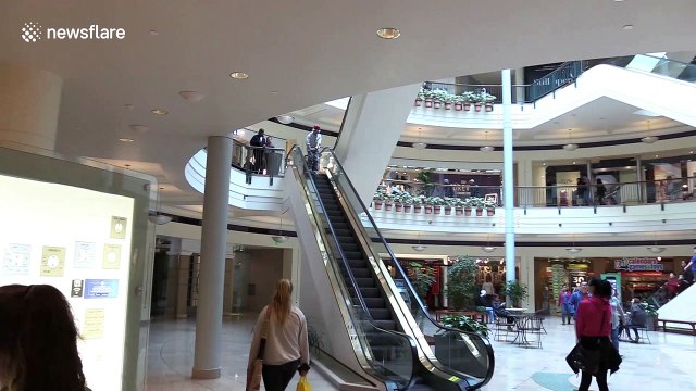 Man in Santa Claus hat descends shopping mall escalator on skis
