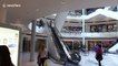Man in Santa Claus hat descends shopping mall escalator on skis
