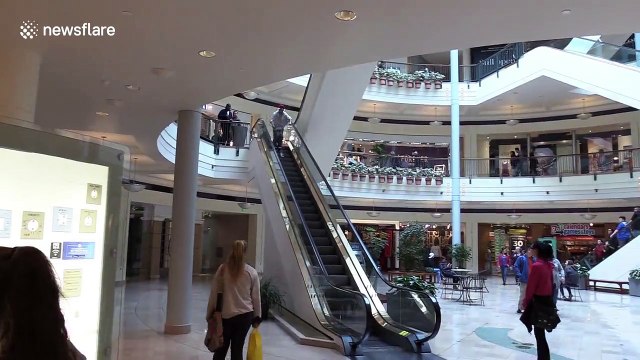 Man in Santa Claus hat descends shopping mall escalator on skis