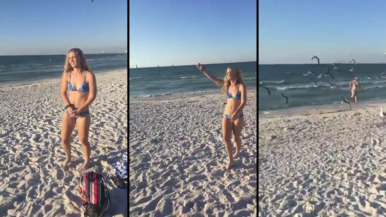 Elle est assaillie par des mouettes en tendant de la nourriture en l'air sur la plage