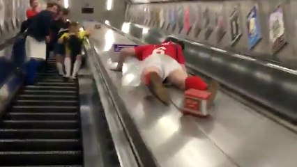 Un supporter de football descend un escalator en glissant.