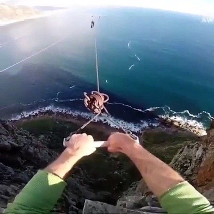 Un homme fait un saut pendulaire du haut d’un rocher et lâche la corde pour sauter dans le vide