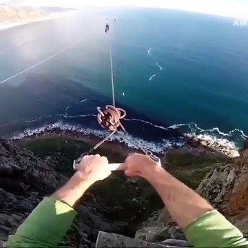 Un homme fait un saut pendulaire du haut d’un rocher et lâche la corde pour sauter dans le vide