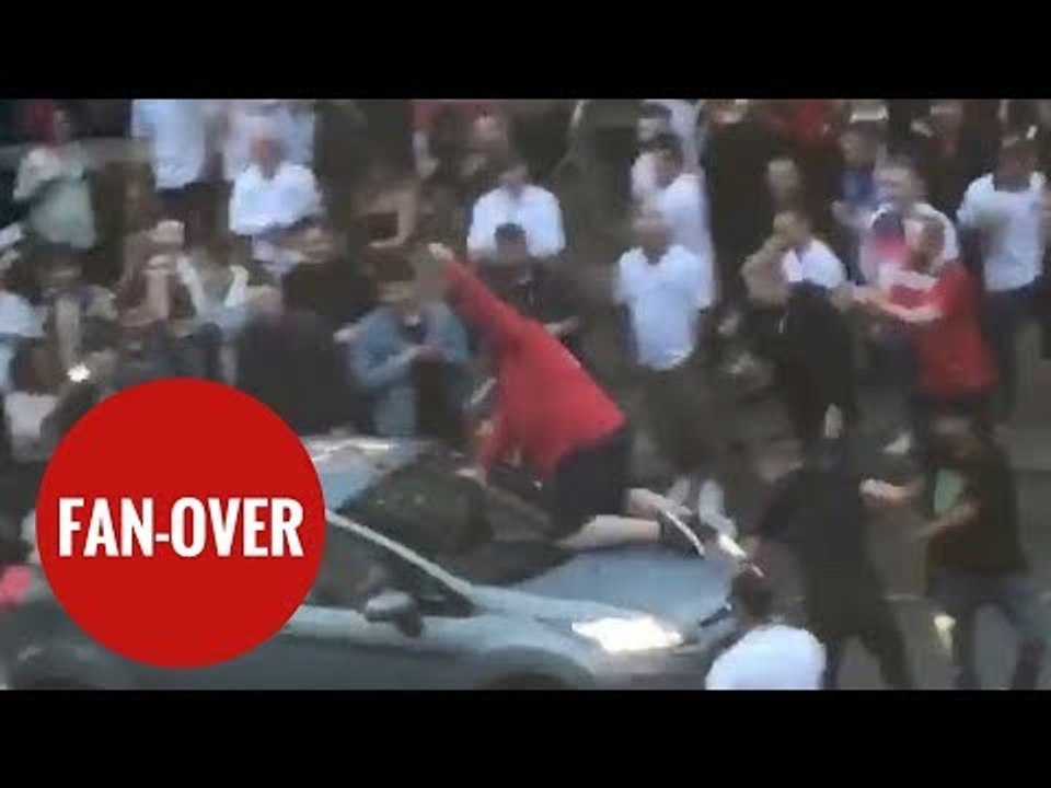Football fan climbs on board MOVING car to cele...
