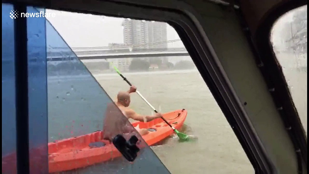 Bare-chested man paddles canoe along swelling river