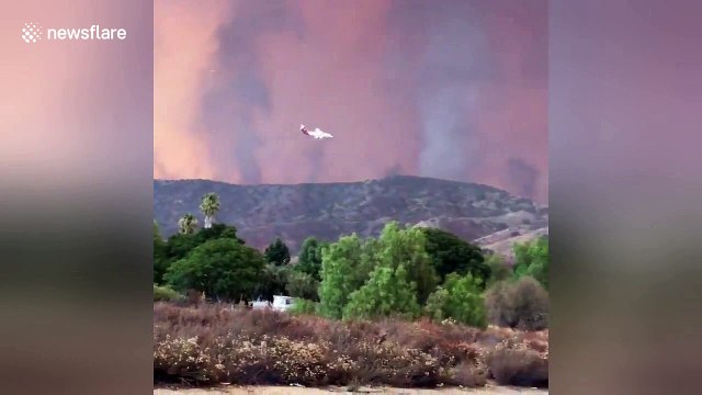 Firefighting plane drop trail of bright red retardant against apocalyptic sky
